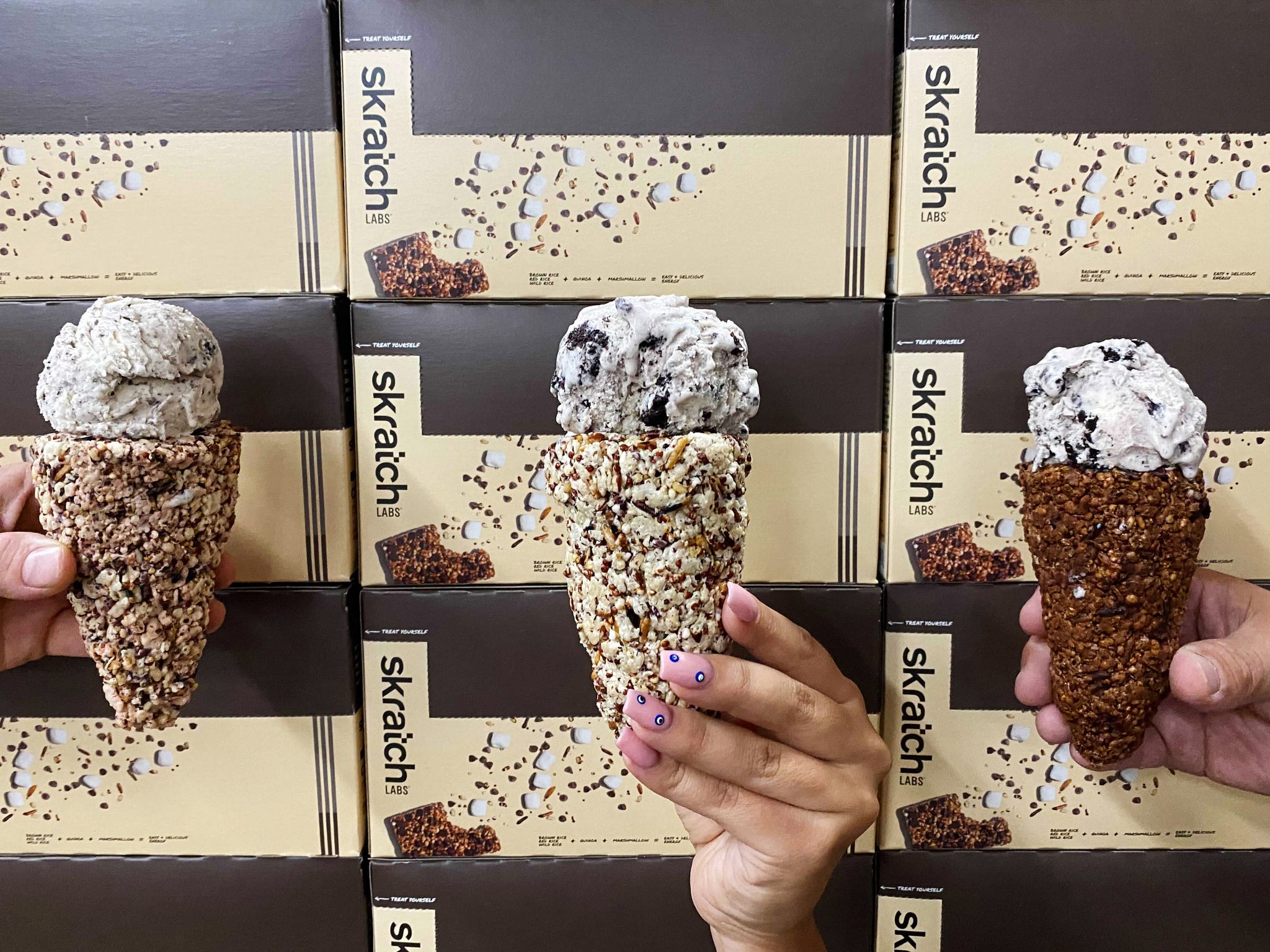 Hands holding ice cream cones in front of skratch crispy boxes